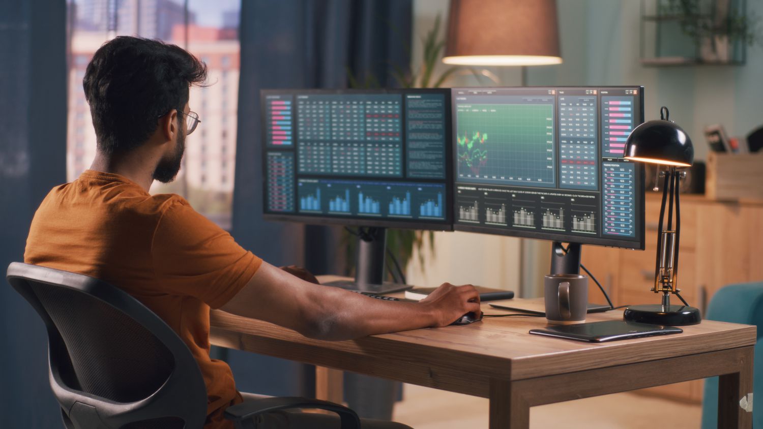 Person seated at a desk, looking at computer monitors showing market trading data