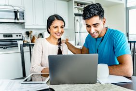 A couple looks at a laptop at their kitchen table