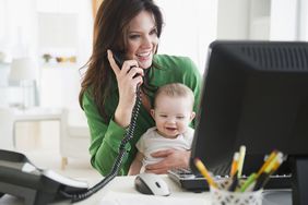 Woman on Phone and at Computer and holding baby while working from home