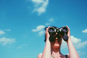 Low Angle View Of Woman Looking Through Binoculars Against Sky