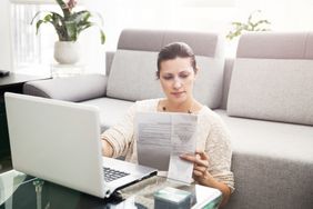 A woman sitting on the floor in front of a laptop, looking at documents