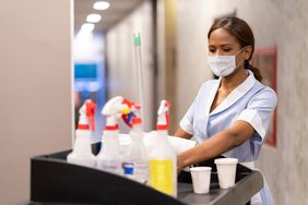 Maid working at a hotel doing room service wearing a facemask and pushing a cart