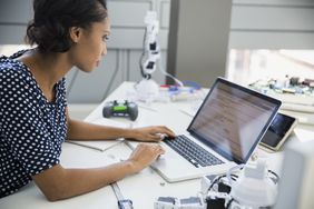 Engineer using laptop at desk with robotics