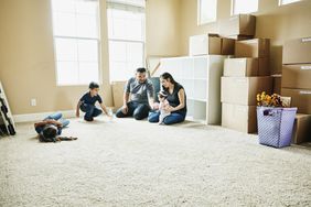 A family sits on the floor of a new home with moving boxes behind them.