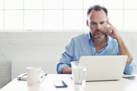 man in collared shirt sitting in all white room, working on computer