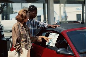 A man and a woman looking at pricing details on a car.