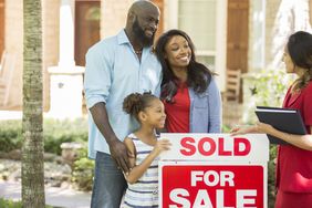 Parents and child standing by a ^aSold^a sign with a real estate agent